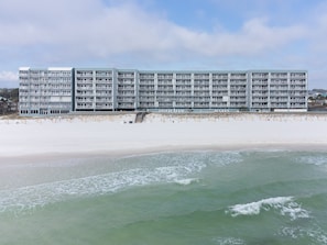 A multi-story hotel with balconies, situated on a sandy beach with ocean views.