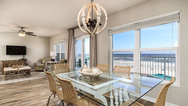 A spacious dining area with a glass table, wicker chairs, and a chandelier.