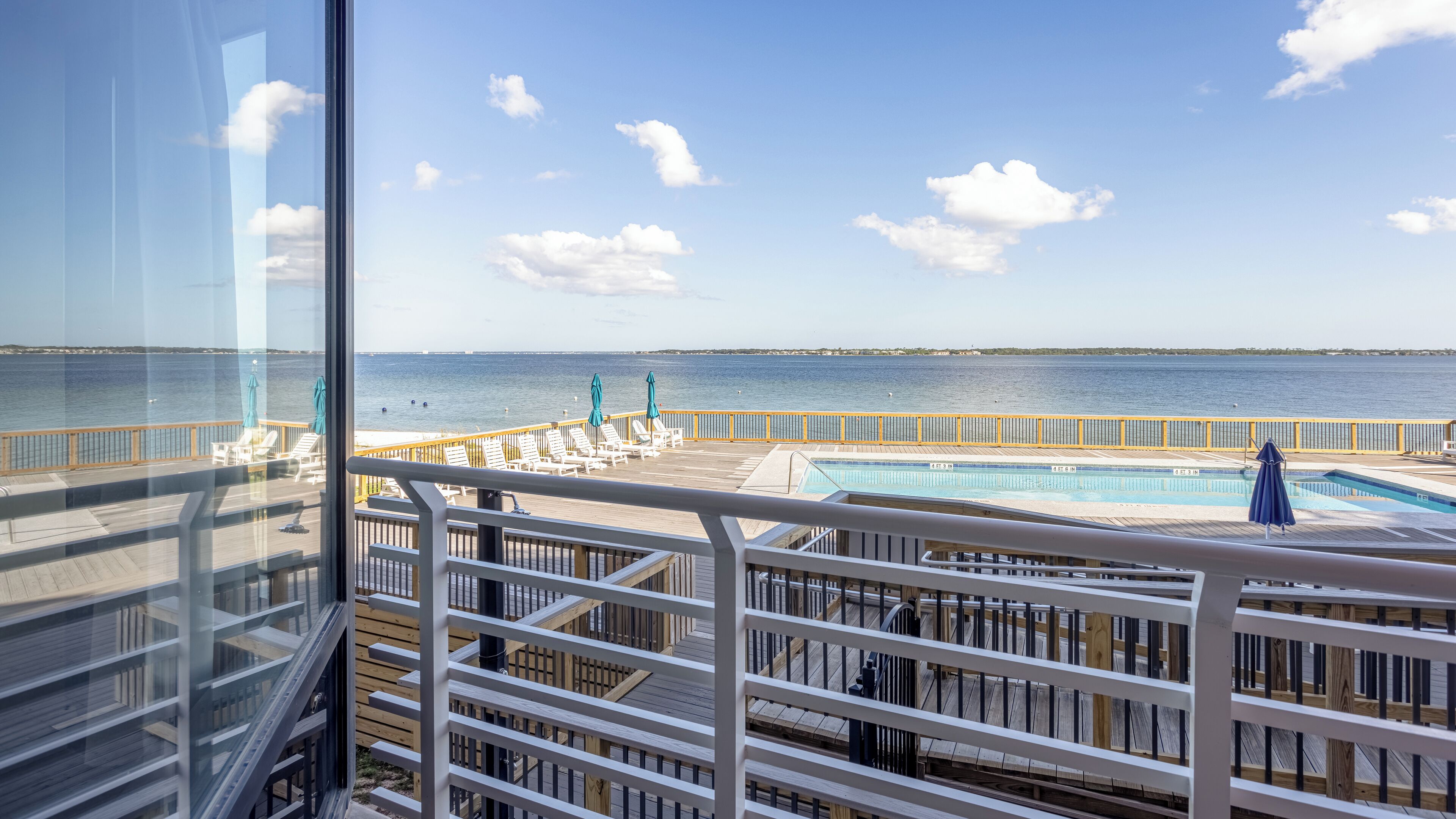 A pool area with a view of the sea, wooden deck, and lounge chairs.