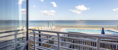 A pool area with a view of the sea, wooden deck, and lounge chairs.