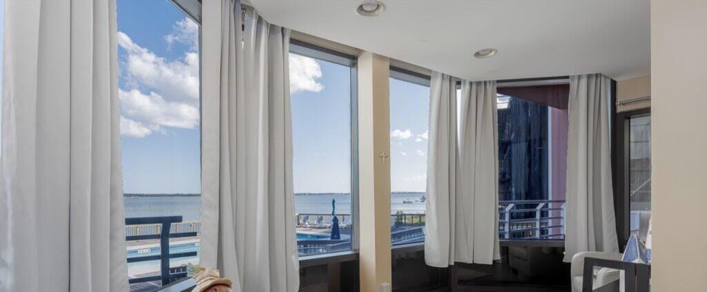 A hotel room with large windows, a view of the sea, and a balcony.