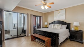 A hotel room with a bed, a bench, a nightstand, a ceiling fan, and a view of the outdoors. - Bayfront Retreat with Pool, Perfect for 6 - PBC108 (Pensacola Beach)