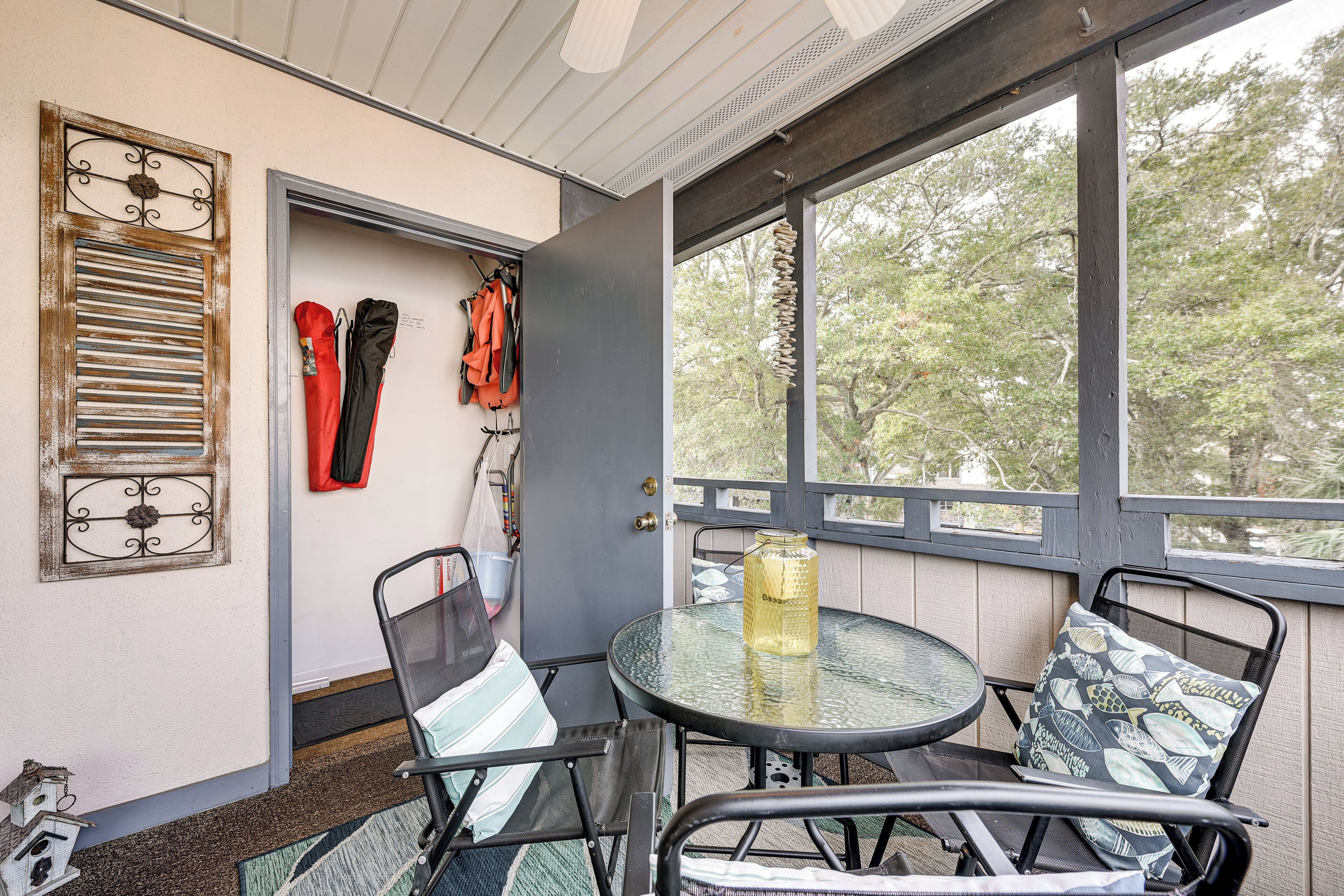 A glass-top table with chairs, a door with a coat rack, and a view of trees through large windows.