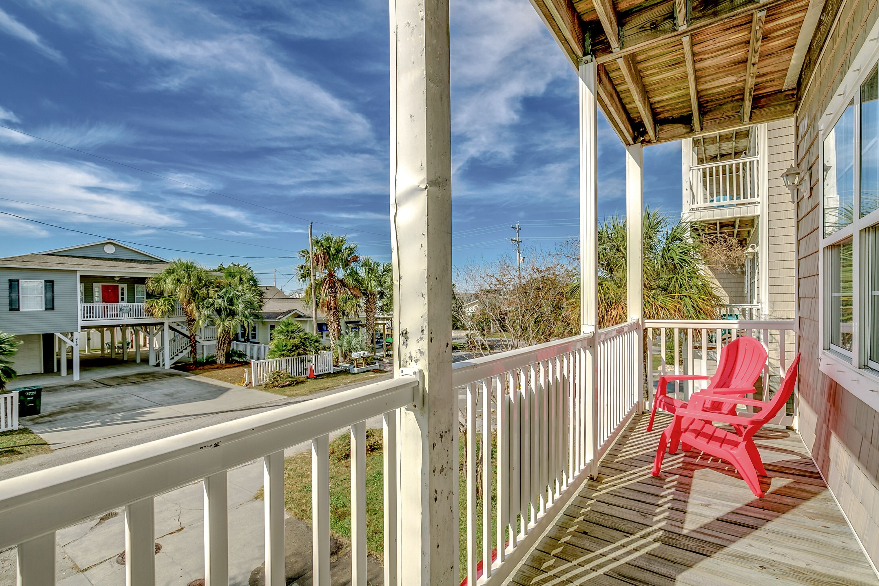 A wooden deck with a red chair, a white railing, and a view of neighboring houses.