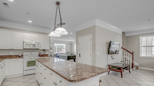 A spacious kitchen with white cabinets, a granite countertop, and a hanging light fixture.