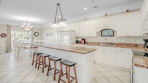 A spacious kitchen with white cabinets, a granite countertop, and a central island with bar stools.