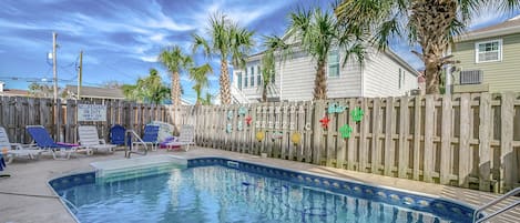 Une piscine dotée de chaises longues et entourée d’une clôture en bois agrémentée d’éléments décoratifs.
