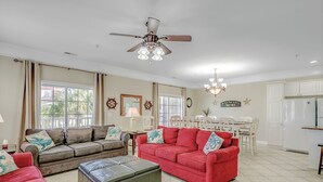 A spacious living room with a red sofa, a brown sofa, and a red armchair. There is a ceiling fan, a chandelier, and a dining table with chairs.