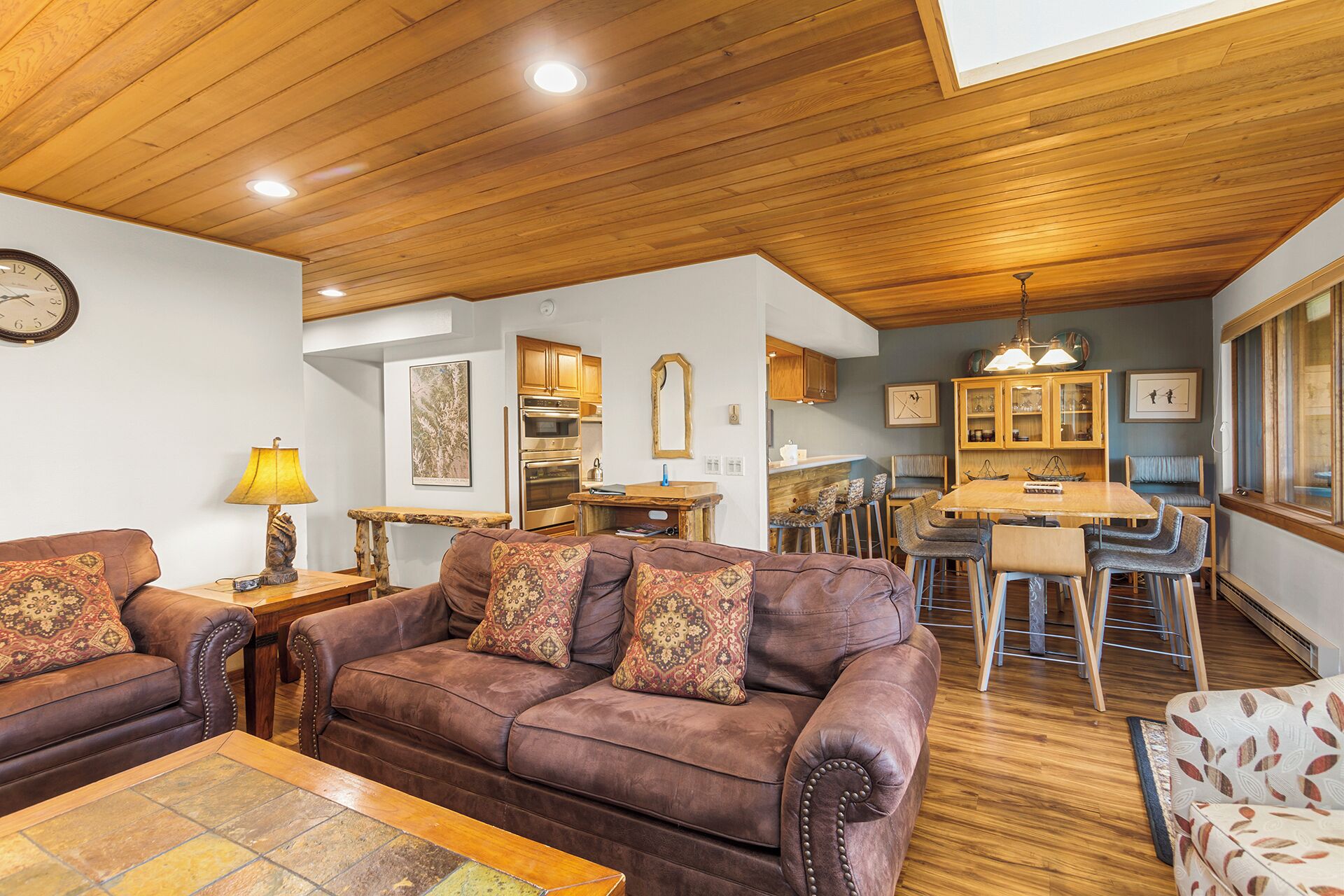 A cozy living room with a brown leather sofa, wooden dining table, and a kitchen in the background.