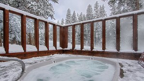 Ein Whirlpool, umgeben von Holzwandungen, mit schneebedeckten Bäumen im Hintergrund.