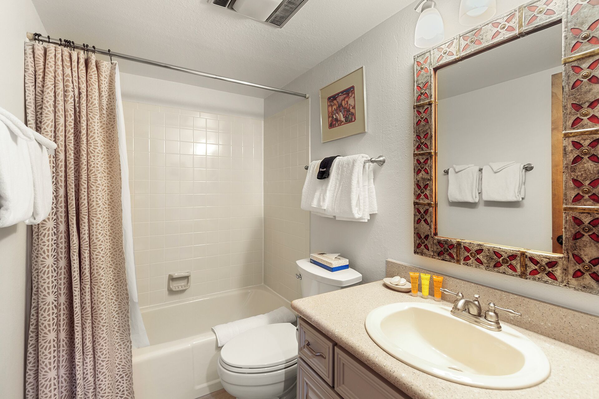 A bathroom with a shower, toilet, sink, and a large mirror with a decorative frame.