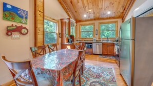 Un interior de madera con una mesa de comedor, sillas, una cocina con refrigerador y ventanas amplias.