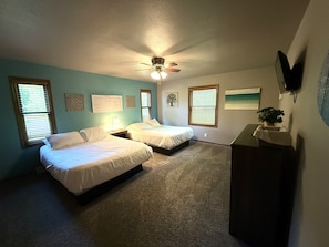 A bedroom with two beds, a ceiling fan, a desk with a plant, and artwork on the walls.