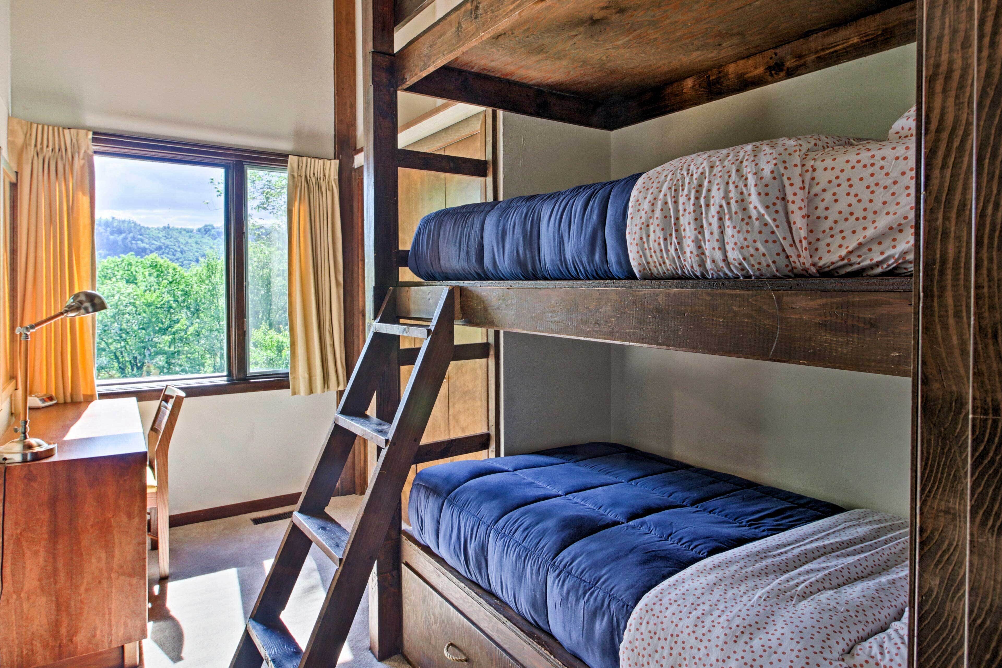 A bunk bed room with a desk and a window overlooking greenery.