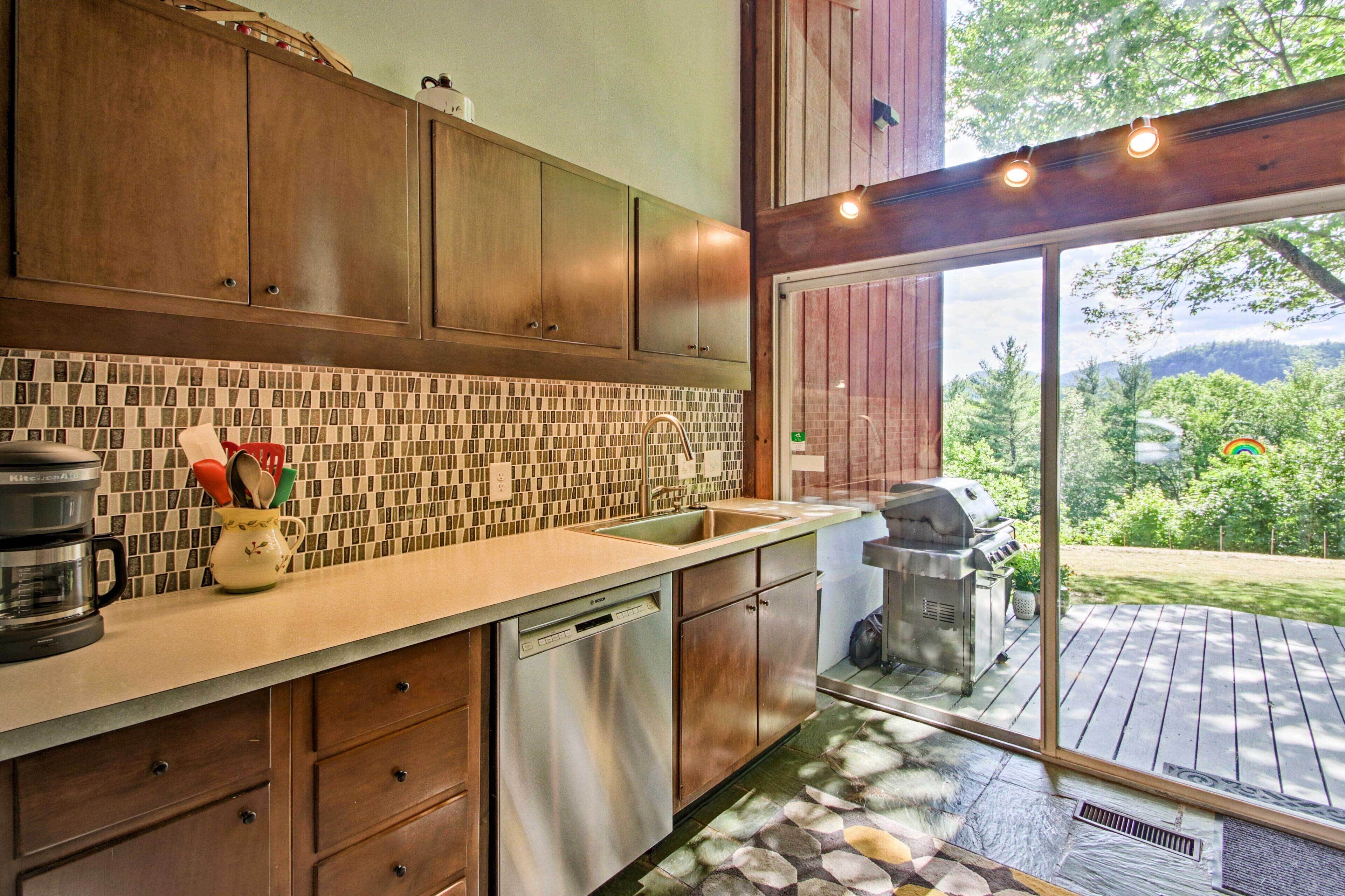 A modern kitchen with wooden cabinets, a tiled backsplash, and a view of a backyard through a sliding glass door.