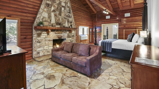 Ein Blockhaus-Interieur mit Kamin aus Stein, einem braunen Sofa, einem Bett und einem Steinfußboden.