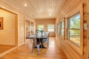 A wooden interior with a dining table and chairs, large windows, and a view of the outdoors. - Private Resort. Pool, Fire Pit,Sleeps up to 50! Great for reunions/events (Wimberley)