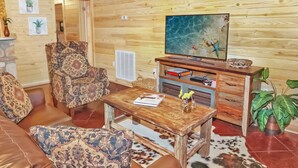 Ein gemütliches Wohnzimmer mit einer Ledersofa, einem gemusterten Sessel, einem Holztisch und einem Flachbildfernseher auf einem Holzständer.