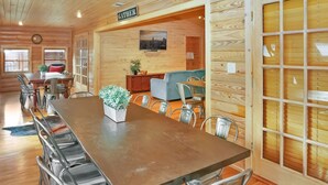 Ein geräumiger Raum mit einem langen Esstisch, Metallstühlen, einer Couch und einem Fernseher an der Wand.