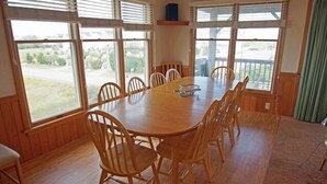 A dining area with a wooden table and chairs, large windows, and a view of the outdoors. - KD906- Semi-OF, 4 BRs, 2 Living Areas, Crow's Nest and Beautiful Views! (Kill Devil Hills)