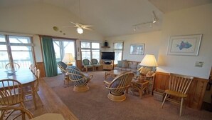 A spacious living room with a dining area, wicker furniture, a ceiling fan, and large windows. - KD906- Semi-OF, 4 BRs, 2 Living Areas, Crow's Nest and Beautiful Views! (Kill Devil Hills)