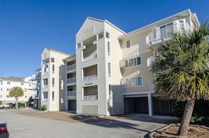 A multi-story residential building with balconies, a garage, and a palm tree in the foreground.