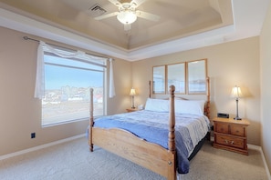 Ein Schlafzimmer mit einem Bett, Nachttischlampen, einem Beistelltisch, einem Fenster mit Blick und einem Deckenventilator.