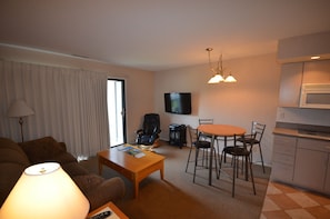 A living room with a sofa, coffee table, TV, and a dining area with chairs and a table.
