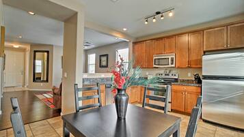 A modern kitchen with wooden cabinets, a stainless steel refrigerator, and a dining area with a table and chairs.