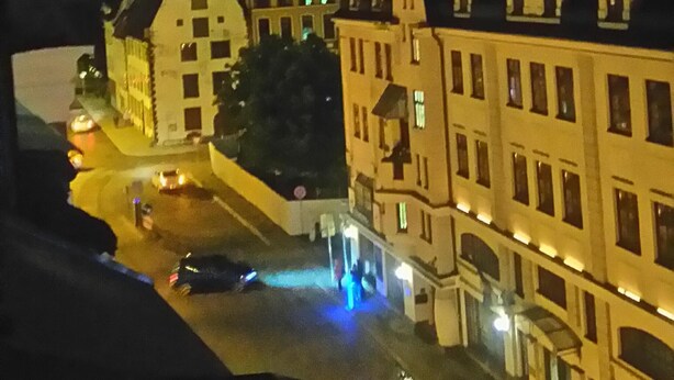 Vista nocturna d'un carrer flanquejat per edificis històrics, alguns amb finestres il·luminades, i una zona d'aparcament ben visible.