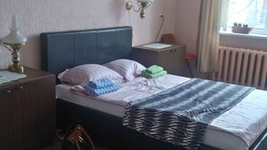 Un dormitori amb un llit, una tauleta de nit, una làmpada i una finestra que dona al exterior.