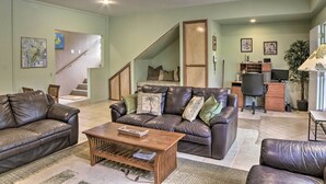 Una sala de estar con un sofá de cuero marrón, una mesa de centro de madera y una escalera que sube a un nivel superior.