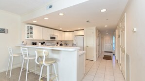 Una cocina moderna con armarios blancos, una isla central con taburetes y luces empotradas en el techo.