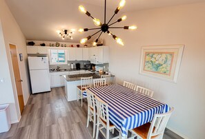 Uma cozinha compacta com armários brancos, uma ilha central e uma área de jantar com toalha de mesa listrada.