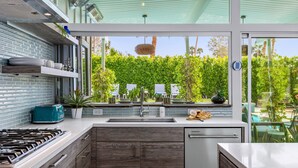 A modern kitchen with a gas stove, a dishwasher, and a view of a lush garden.
