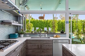 A modern kitchen with a gas stove, a dishwasher, and a view of a lush garden.