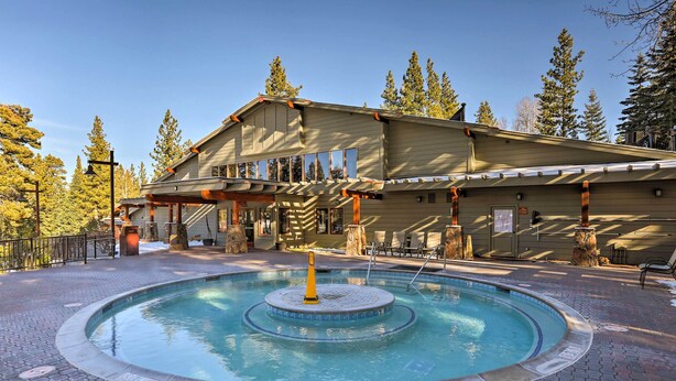 A pool area with a circular fountain, a building with a sloped roof, and surrounding trees. - Ski-In/Ski-Out Northstar Condo Near Lake Tahoe! (Truckee)