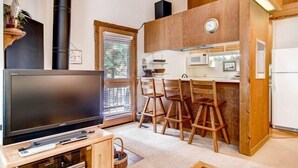 A compact living space with a TV, wooden bar stools, a kitchen area, and a large window. - Ski-In/Ski-Out Northstar Condo Near Lake Tahoe! (Truckee)