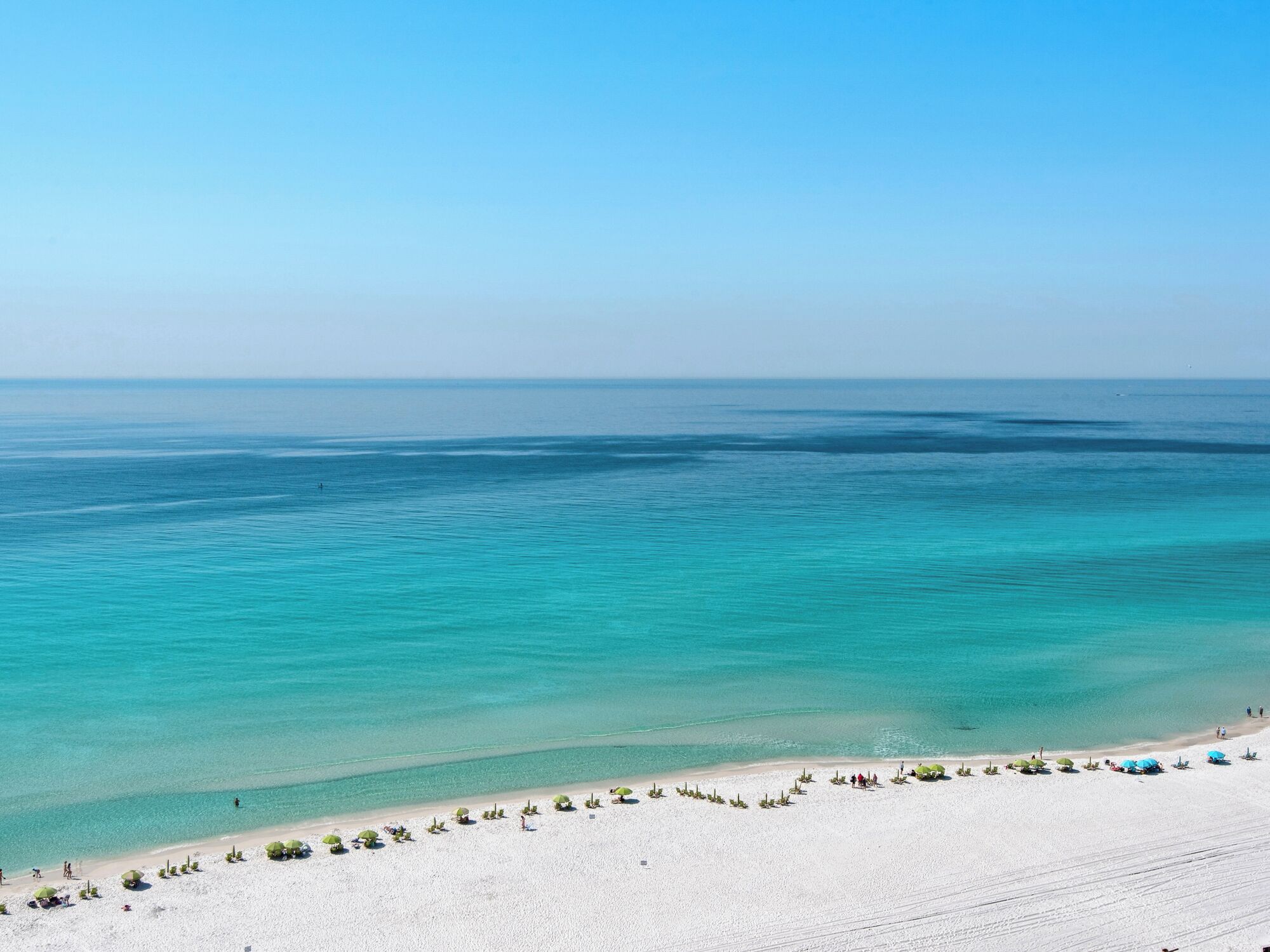 A beach with clear turquoise water, white sand, and several umbrellas.