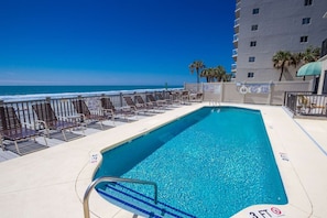 A pool with a 3 FT depth marker, surrounded by lounge chairs and a view of the ocean.