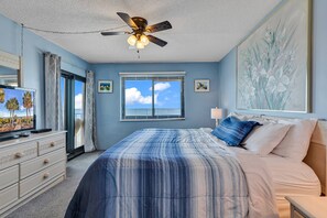 A bedroom with a bed, a ceiling fan, a TV, and a window with blinds.