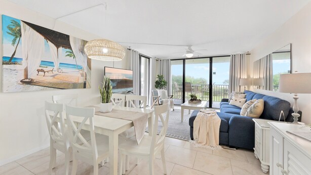 A spacious living room with a dining area, a sofa set, and a large painting of a beach scene. - ☀️ Sun-Kissed Escape  l  Oceanfront Condo w/ Private Balcony l Pool, Hot Tub & Tennis (Cape Canaveral)
