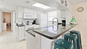 A modern kitchen with white cabinetry, a central island, and a green kettle. - ☀️ Sun-Kissed Escape  l  Oceanfront Condo w/ Private Balcony l Pool, Hot Tub & Tennis (Cape Canaveral)