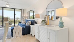 A modern bedroom with a blue sofa, white dresser, and a large mirror. - ☀️ Sun-Kissed Escape  l  Oceanfront Condo w/ Private Balcony l Pool, Hot Tub & Tennis (Cape Canaveral)
