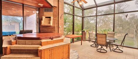 A modern indoor patio with a hot tub, wooden steps, and a seating area with chairs and a table.
