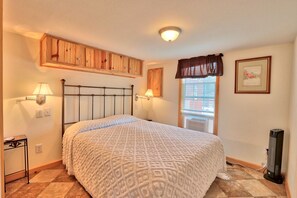 A bedroom with a bed, two bedside lamps, a wooden headboard, a window with a curtain, a framed picture on the wall, and a heater on the floor. - Amazing Ranch Sleeps 42 Plus! Located On 75 Acres With A Pool And Barn (Wimberley)