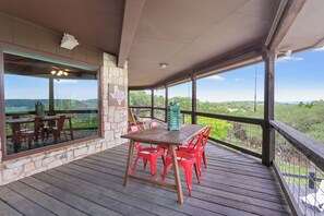 A covered outdoor area with a wooden deck, a table with chairs, and a view of the landscape. - On Top of the World  I Minutes from beautiful Canyon Lake (Wimberley)