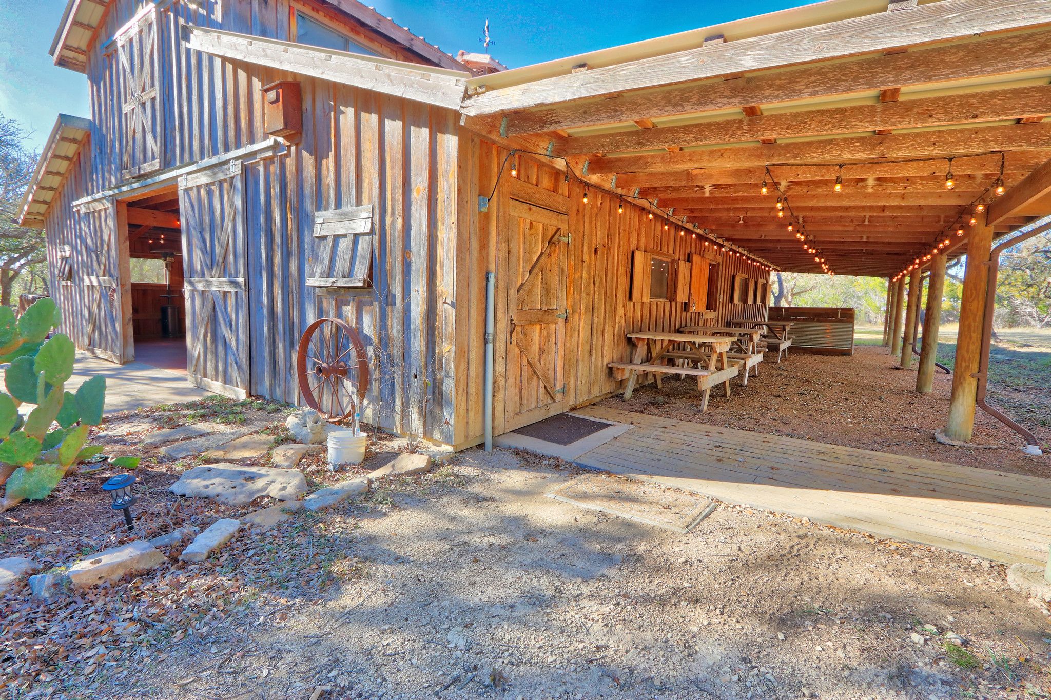 A rustic wooden building with a covered patio area, a large wooden wheel, and a rustic outdoor seating area.