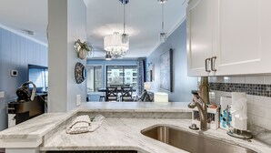 A modern kitchen with a marble countertop, stainless steel sink, and a built-in dishwasher. There is a dining area visible in the background with a table and chairs. - Walk to Beach: Hilton Head Resort Condo w/ Pools! (Hilton Head Island)