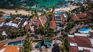 Vue aérienne d’un complexe hôtelier doté de plusieurs piscines, d’une plage et de palmiers.